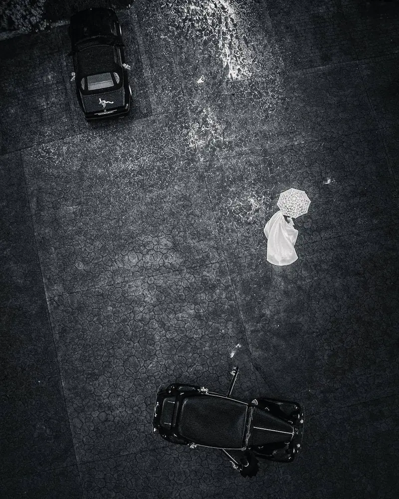 Fotografía aérea en blanco y negro de una boda: la novia con paraguas entre dos coches clásicos, por Josu Izarra Fotógrafos en Vitoria-Gasteiz