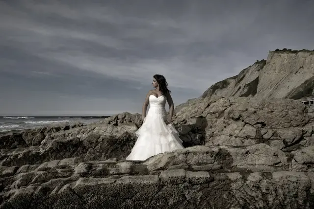 Novia sobre las rocas de la costa vasca con cielo dramático, postboda de Josu Izarra