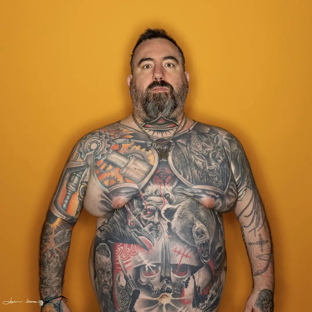 Retrato de estudio de un hombre con el torso tatuado sobre fondo ocre, fotografía de Josu Izarra en Vitoria-Gasteiz