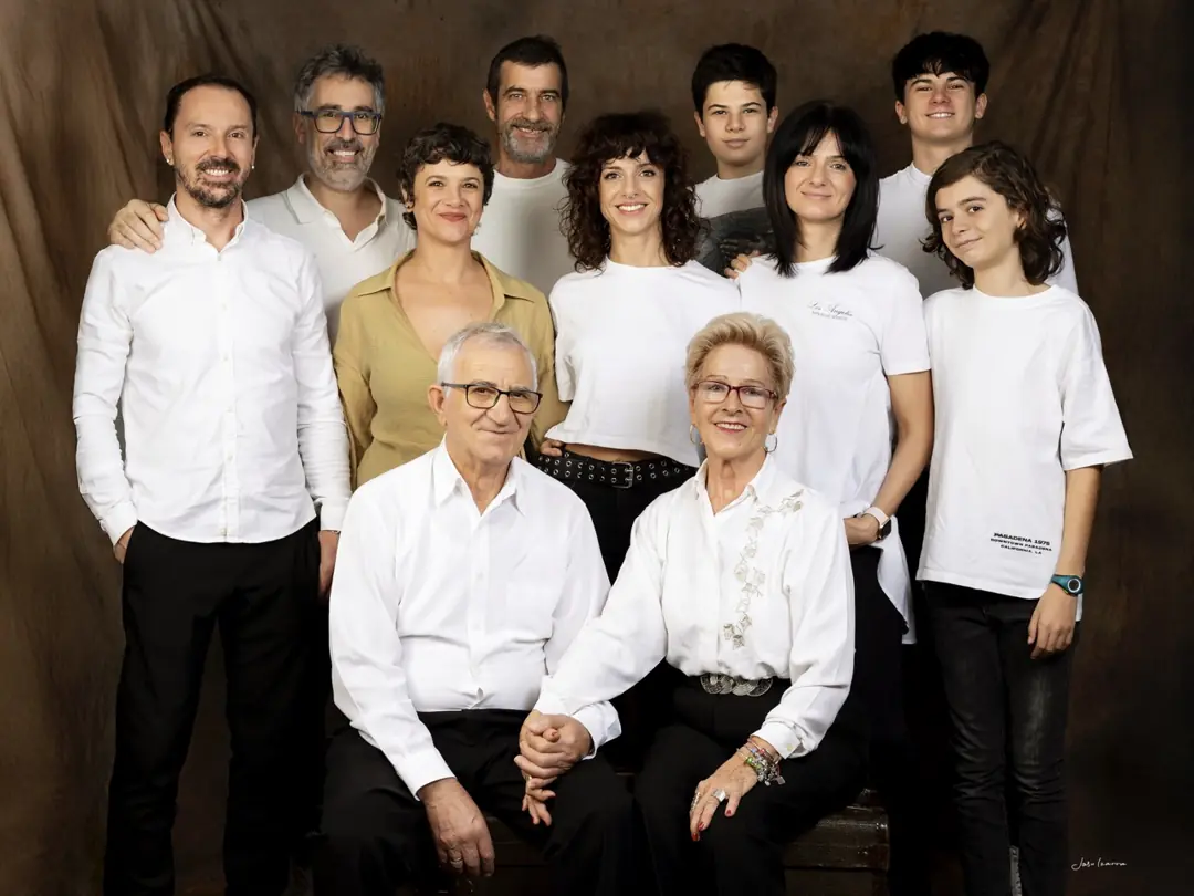 Retrato de familia de estudio de varias generaciones vestidas de blanco sobre fondo marrón, por Josu Izarra